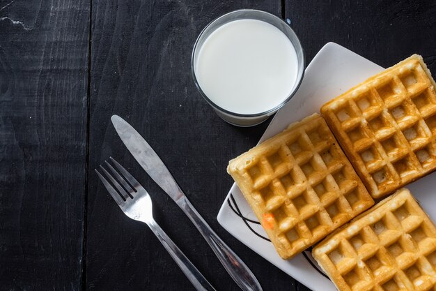 Nahaufnahme Schuss von quadratischen Waffeln und Milchglas auf einem Holztisch