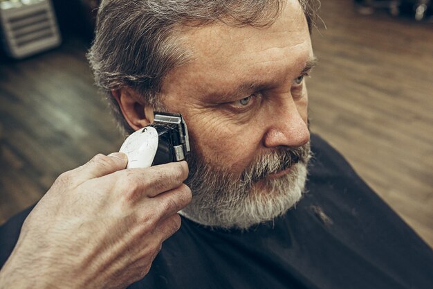 Nahaufnahme-Seitenansichtporträt des hübschen älteren bärtigen kaukasischen Mannes, der Bartpflege im modernen Friseursalon erhält.