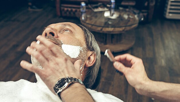 Nahaufnahme seitlicher Draufsicht schöner älterer bärtiger kaukasischer Mann, der Bartpflege im modernen Friseursalon erhält.