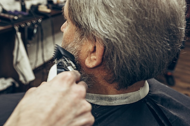 Nahaufnahme seitlicher rückansicht schöner älterer bärtiger kaukasischer mann, der bartpflege im modernen friseursalon erhält.