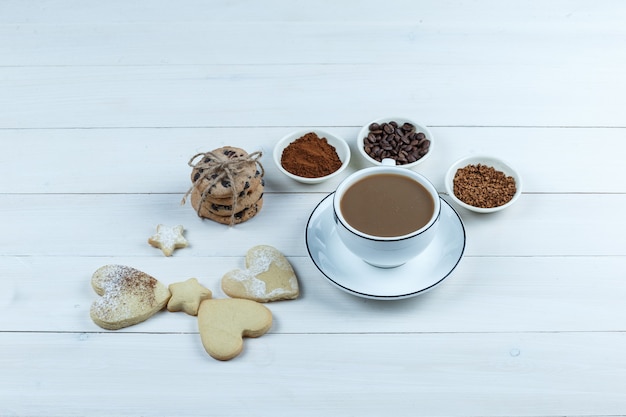 Nahaufnahme tasse kaffee mit kaffeebohnen, instantkaffee, kakao, verschiedene arten von keksen auf weißem holzbrett hintergrund. horizontal