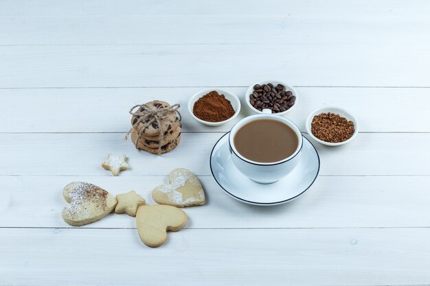 Nahaufnahme Tasse Kaffee mit Kaffeebohnen, Instantkaffee, Kakao, verschiedene Arten von Keksen auf weißem Holzbrett Hintergrund. horizontal