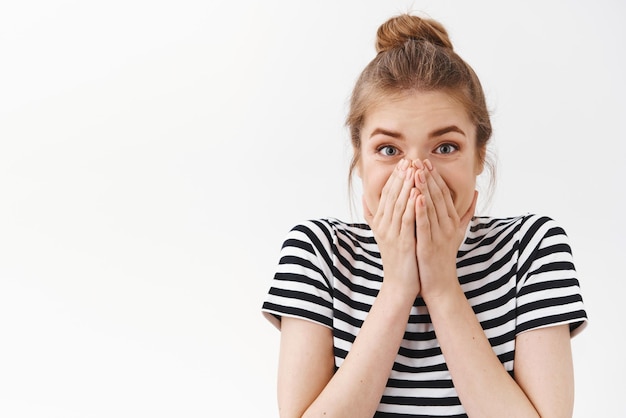 Kostenloses Foto nahaufnahme überrascht erstaunt sprachlos gutaussehende frau in gestreiftem t-shirt mit unordentlichem brötchen bedeckt den mund, als sie albern und erstaunt auf den weißen hintergrund des fantastischen geschenkständers reagiert kopierraum