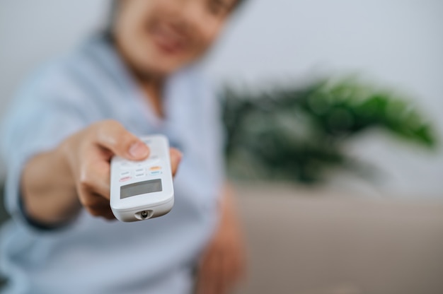 Nahaufnahme und selektive Fokushand der Frau, die die Fernbedienung hält und verwendet, um die Klimaanlage im Wohnzimmer zu Hause zu öffnen