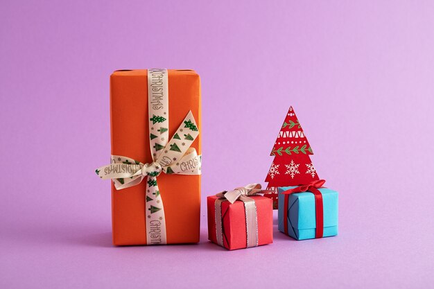 Nahaufnahme von bunten Geschenkboxen und einem Papierweihnachtsbaum im lila Hintergrund