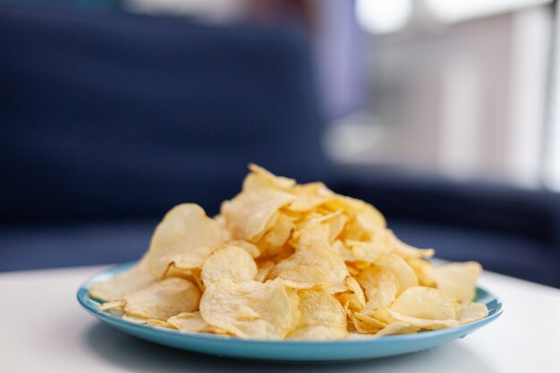 Nahaufnahme von Chips Snack auf Couchtisch sitzen. Modernes Wohnzimmer mit niemandem herein mit blauen Möbeln und Wänden, schön verziert Ziemlich einfache Einrichtung der Wohnung. Elegante Retro-Dekoration, gemütlich.