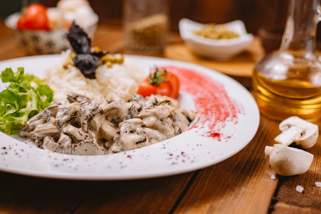 Nahaufnahme von cremigem Pilz serviert mit Reis, garniert mit Salattomate und dunklen Basilikumblättern