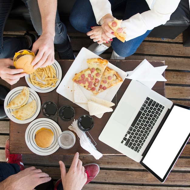 Nahaufnahme von den freunden, die snack mit getränken und laptop auf tabelle essen