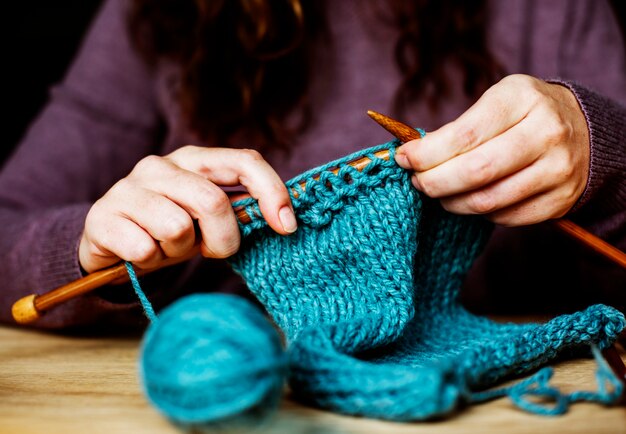 Nahaufnahme von den Händen, die auf Holztisch stricken