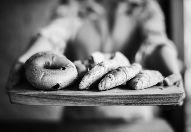 Nahaufnahme von den Händen, die frisches gebackenes Brot auf hölzernem Behälter halten