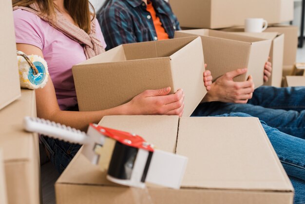 Nahaufnahme von den jungen Paaren, die in der Hand Pappschachteln an ihrem neuen Haus halten