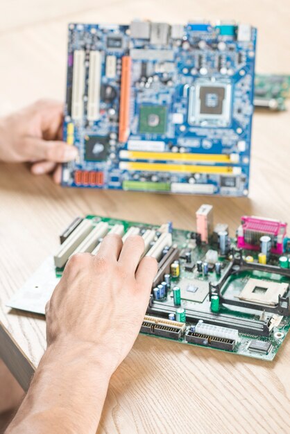 Nahaufnahme von den männlichen Händen, die üben, Motherboard auf Holztisch zu reparieren