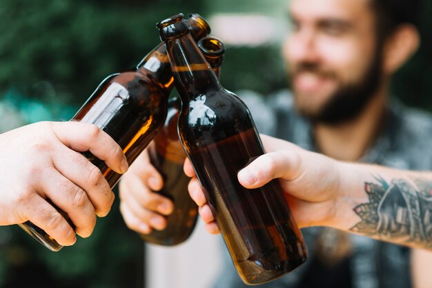 Nahaufnahme von Freunden klirren die Bierflaschen an draußen