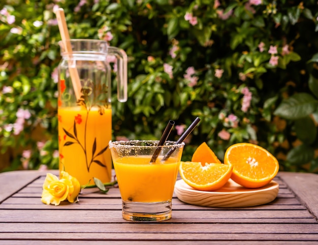 Nahaufnahme von frischem Orangensaft mit geschnittenen Orangenscheiben auf einem Holztisch im Freien