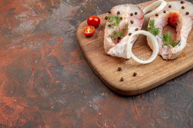 Nahaufnahme von frischen rohen Fischen und Paprika-Zwiebelgrün-Tomaten auf Holzbrett auf Mischfarboberfläche