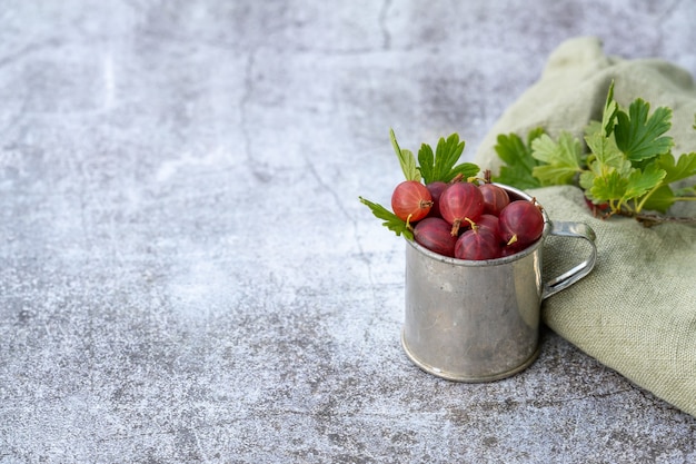 Nahaufnahme von frischen roten stachelbeeren in einem kleinen eimer, platziert auf einer grunge-oberfläche