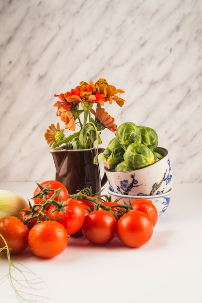 Nahaufnahme von frischen roten Tomaten; Rosenkohl und Blumen auf weißer Tischplatte