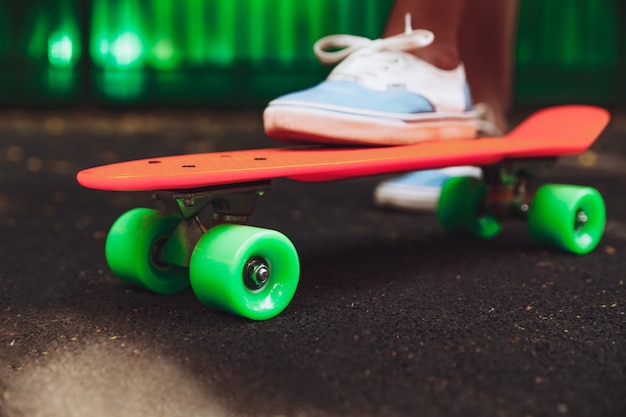 Nahaufnahme von füßen von mädchen turnschuhen reitet auf orange penny skateboard auf asphalt