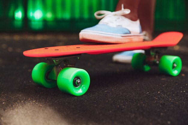 Nahaufnahme von Füßen von Mädchen Turnschuhen reitet auf orange Penny Skateboard auf Asphalt