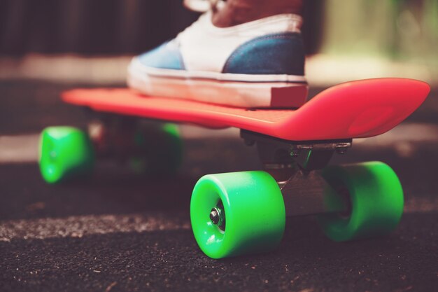 Nahaufnahme von Füßen von Mädchen Turnschuhen reitet auf orange Penny Skateboard auf Asphalt