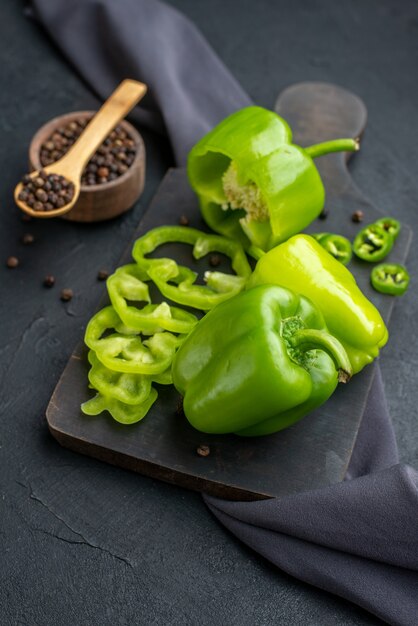 Nahaufnahme von ganzen geschnittenen gehackten grünen Paprika auf Holzbrett auf dunkler Farboberfläche