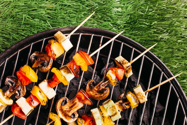 Nahaufnahme von gegrillten aufsteckspindeln mit fleisch und gemüse auf grill über matte des grünen grases