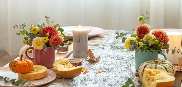 Nahaufnahme von gemütlichen Dekordetails eines festlichen Herbstesstisches mit Kürbissen, Blumen und Kerzen.