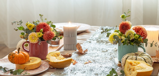 Nahaufnahme von gemütlichen Dekordetails eines festlichen Herbstesstisches mit Kürbissen, Blumen und Kerzen.