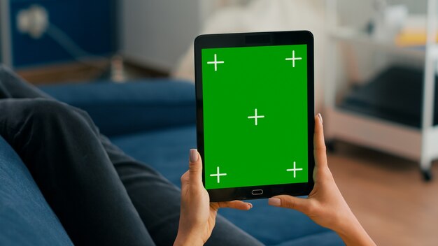 Nahaufnahme von Geschäftsfrauenhänden, die Tablet-Computer mit Mock-up-Greenscreen-Chroma-Key-Display auf dem Sofa halten. Freiberufler, der ein isoliertes Touchscreen-Gerät zum Surfen in sozialen Netzwerken verwendet