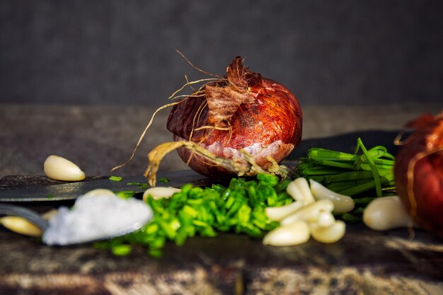 Nahaufnahme von geschnittenen Zwiebeln, Schnittlauch, Zwiebeln, Knoblauch und einem Teelöffel Salz auf einer Holzoberfläche