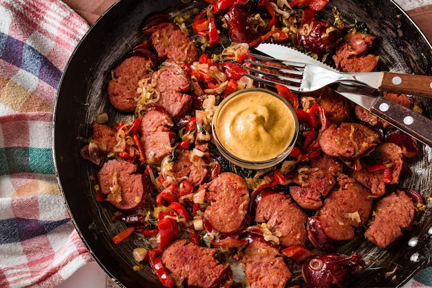 Nahaufnahme von geschnittener Wurst und Mischung von frischem Gemüse, das in der rustikalen Pfanne mit Senf gebraten wird