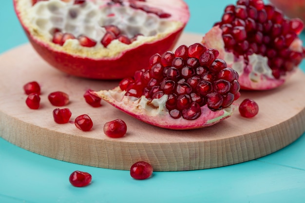 Nahaufnahme von Granatapfelstücken und Beeren mit Granatapfelhälfte auf Schneidebrett auf blauer Oberfläche