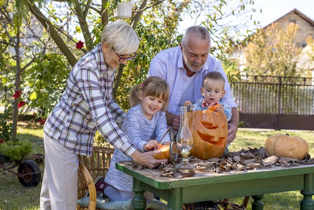 Nahaufnahme von Großeltern, die Kindern helfen, einen Kürbis für Halloween zu schnitzen