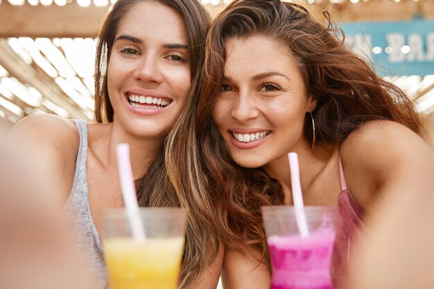 Nahaufnahme von gut aussehenden europäischen Frauen haben Spaß, feiern etwas, trinken Sommercocktails, machen Selfie, teilen Fotos in sozialen Netzwerken.