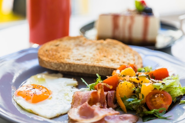 Nahaufnahme von halbem Spiegelei; Speck; Salat und Toast auf grauer Keramikplatte