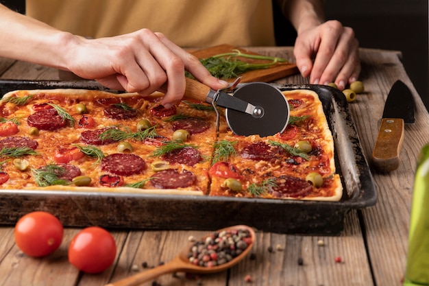 Nahaufnahme von Hand, die Pizza schneidet