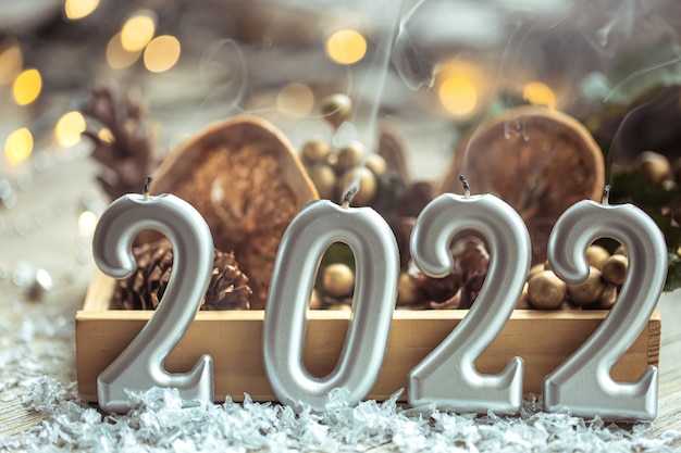 Nahaufnahme von Kerzen in Form der Zahlen 2022 auf unscharfem Hintergrund mit Weihnachtsdekor und Bokeh.