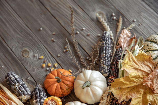 Nahaufnahme von Kürbis, Mais und Herbstlaub auf einem hölzernen Hintergrund, Draufsicht, Kopienraum.
