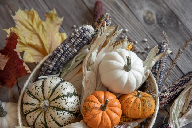 Nahaufnahme von Kürbis, Mais und Herbstlaub auf einem hölzernen Hintergrund, rustikaler Stil.