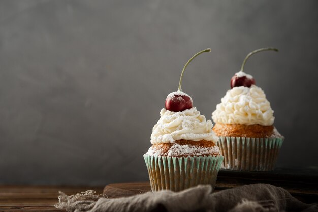 Nahaufnahme von leckeren Cupcakes mit Sahne, Puderzucker und einer Kirsche oben drauf