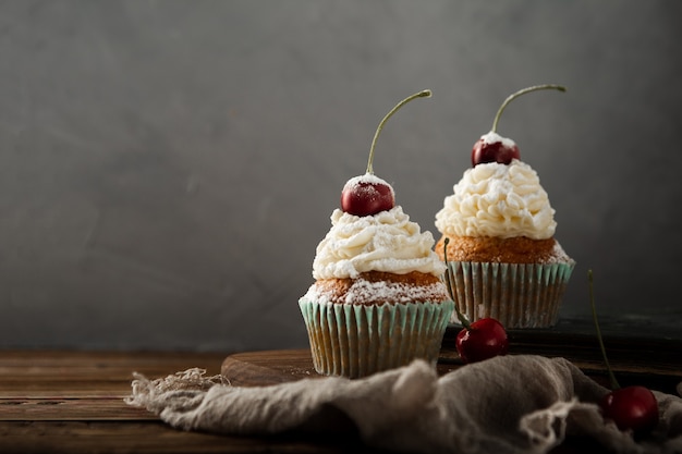 Nahaufnahme von leckeren Cupcakes mit Sahne, Puderzucker und einer Kirsche oben drauf