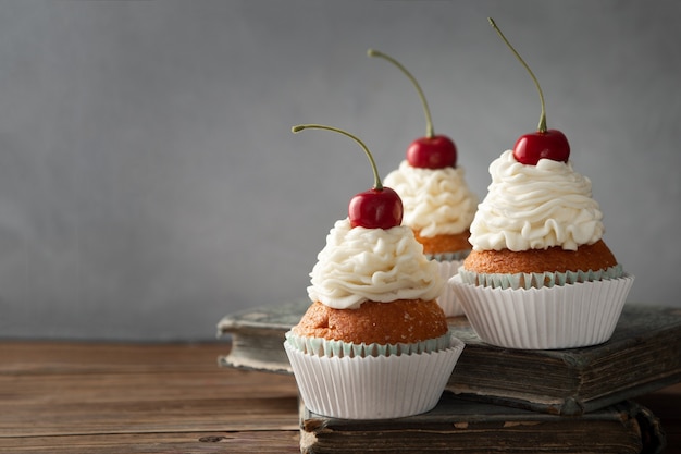 Nahaufnahme von leckeren Cupcakes mit Sahne und Kirsche oben auf Büchern