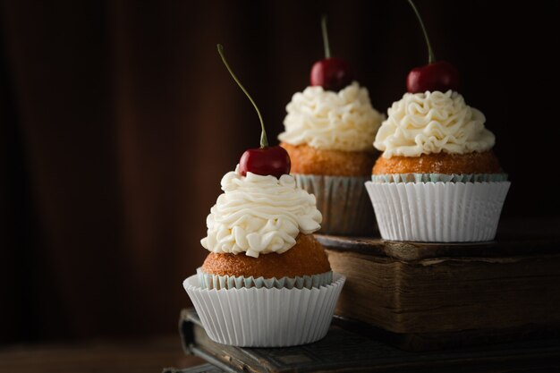 Nahaufnahme von leckeren Cupcakes mit Sahne und Kirschen auf Vintage-Büchern