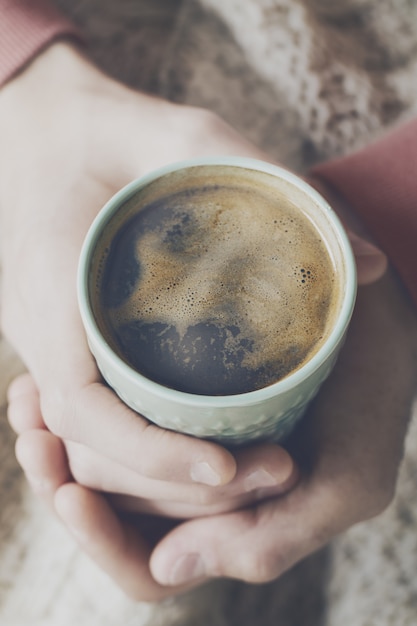 Nahaufnahme von leckeren Kaffee Espresso mit leckeren gelben Schaum in grün Keramik Tasse. Männliche Hände halten warmes Heißgetränk.