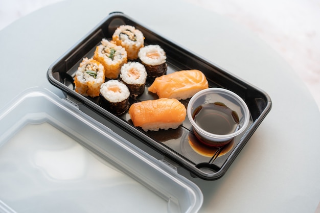 Nahaufnahme von leckeren Sushi-Rollen in einer Plastikbox auf einer weißen Oberfläche