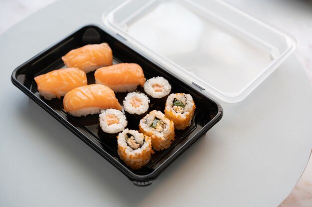 Nahaufnahme von leckeren Sushi-Rollen in einer Plastikbox auf einer weißen Oberfläche