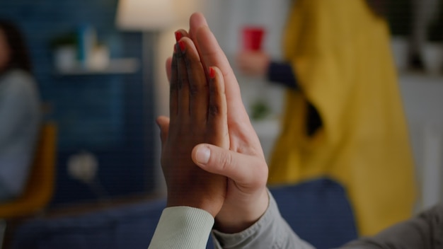 Nahaufnahme von multiethnischen Freunden, die während der Feierparty High Five geben, während sie spät auf dem Sofa sitzen ...