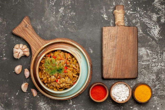 Nahaufnahme von oben appetitliche grüne Bohnen appetitliche grüne Bohnen und Tomaten auf dem Holzbrett Schüsseln mit Gewürzen Knoblauch und Schneidebrett