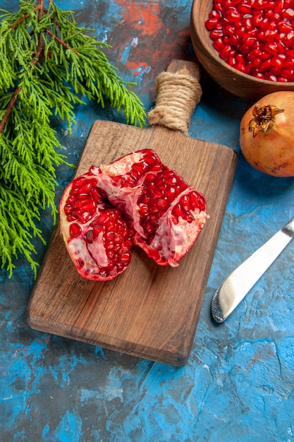 Nahaufnahme von oben ein geschnittener Granatapfel und ein Tafelmesser auf einem Schneidebrett Granatapfelkerne in einer Schüssel und Granatäpfel auf blauem Hintergrund