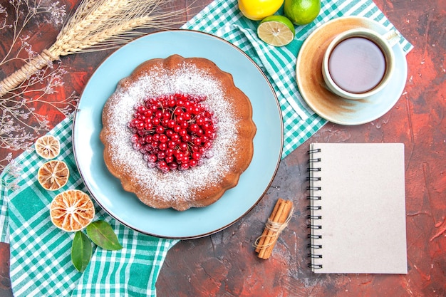 Nahaufnahme von oben ein Kuchen ein Kuchen mit Beeren Limetten auf der Tischdecke eine Tasse Tee weißes Notizbuch